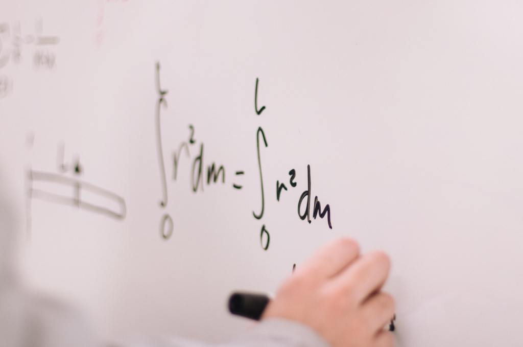 Person writing math equations on a whiteboard. 