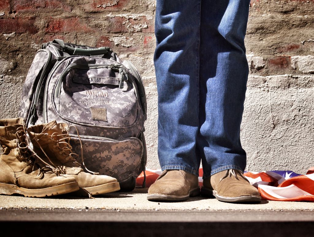 A person standing near military backpack and boots. 