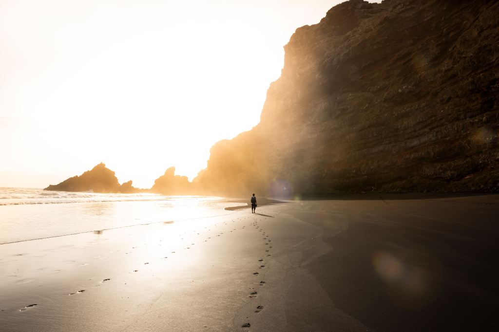Man on shore near rock formation.
