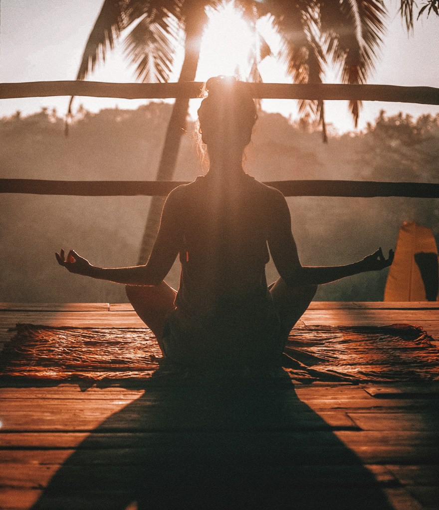 Woman in black tank top meditating on brown wooden dock during daytime.