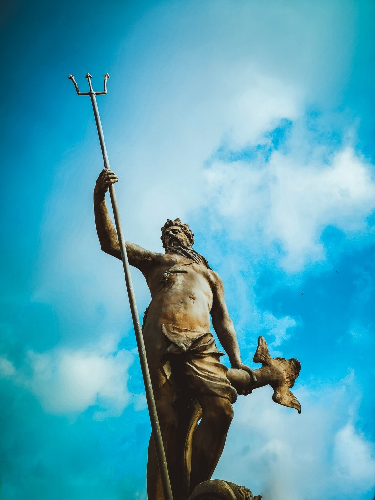 Man holding trident statue under white clouds at daytime. 